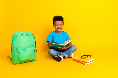 Full length photo of positive charming preteen boy wear blue t-shirt reading fairytails isolated yellow color backgroundの写真素材