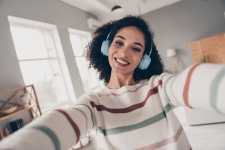 Photo of adorable sweet lady dressed striped pullover earphones recording vlog indoors apartment roomの写真素材