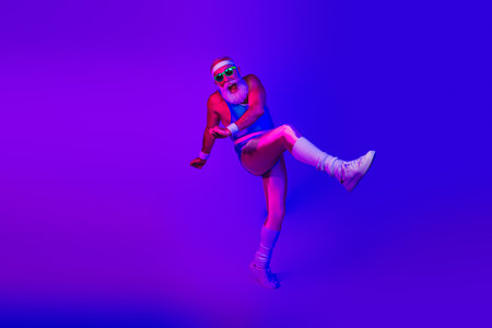 Energetic retro fitness dancer shows bold style as he leaps in neon purple and blue lighting for wellness lifestyle and fun promotionの写真素材
