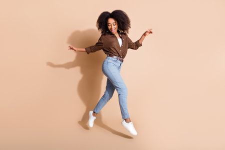 Full length photo of satisfied gorgeous girl wear brown blouse jeans flying dancing look down on legs isolated on pastel color backgroundの写真素材