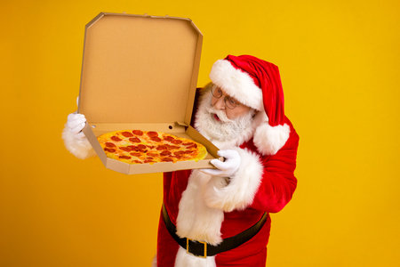 Santa delivers a hot pepperoni pizza in a cardboard box against a bright yellow background for a festive holiday scene and fun family momentの写真素材