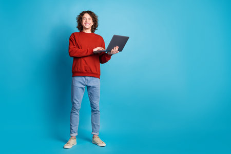 Full length photo of cheerful positive guy dressed pullover typing gadget empty space isolated blue color backgroundの写真素材