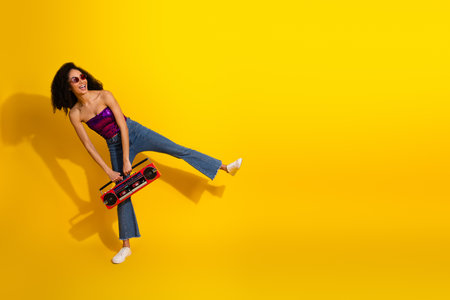Young glamorous woman in a purple sequined top kicks her leg while holding a red boombox against a vivid yellow backgroundの写真素材