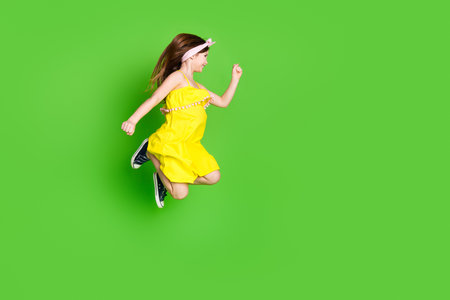 Full length photo of adorable lovely small girl wear pin up dress jumping high running empty space isolated green color backgroundの写真素材