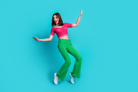 Full length photo of funny woman dressed pink top green retro pants stand on tiptoes look empty space isolated on blue color backgroundの写真素材