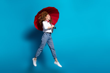 Photo portrait of young lady jump look empty space hold umbrella wear trendy white garment isolated on blue color backgroundの写真素材