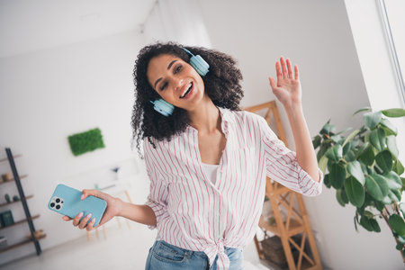 Photo of adorable sweet lady wear white shirt earphones having fun listening songs modern device indoors room home houseの写真素材
