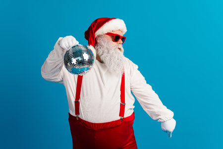 Santa with disco ball dances in a festive costume against a blue background perfect for christmas marketing and holiday promotionの写真素材