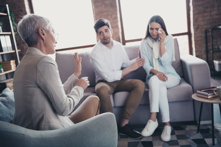 Portrait of young married couple sitting sofa consultation visit psychotherapist loft interior office indoorsの写真素材