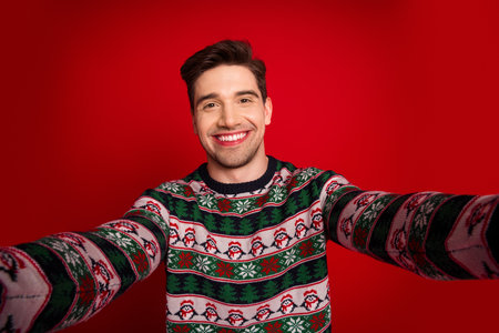 Playful selfie moment with a festive christmas sweater man smiling big against a bold red backgroundの写真素材