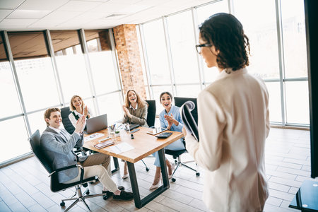 Business team in a modern office applauding a presentation by a colleague, showcasing teamwork, collaboration, and professional successの写真素材