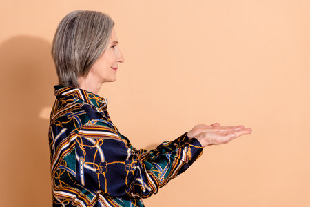 Side profile photo of cheerful person with bob hairdo wear blouse look at object on palms empty space isolated on beige color backgroundの写真素材