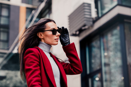 Stylish businesswoman in a red coat enjoying a bright urban day as she walks confidently through the city streets.の写真素材