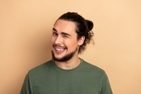 Young man winking and smiling in a green t shirt against a beige background displaying casual fashion and friendly advertising vibeの写真素材