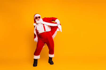 Santa in red costume with cape and sunglasses striking a playful yellow background festive Christmas themed stock photoの写真素材
