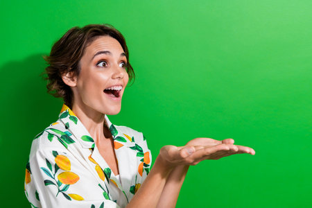 Photo of excited shiny girl dressed print shirt looking showing arms empty space isolated green color backgroundの写真素材