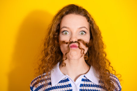 Playful red haired woman makes mustache face against bright yellow background wearing striped shirtの写真素材