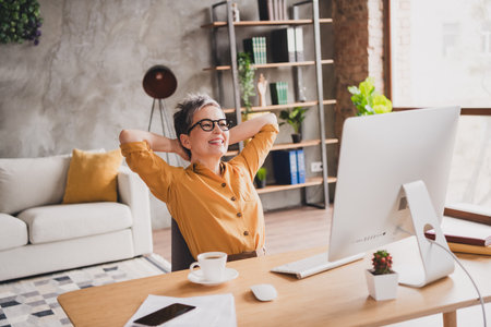 Photo of pretty retired woman hands behind head dressed yellow formalwear modern workplace working home distance officeの写真素材