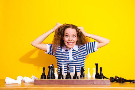 Young woman with curly hair grins while playing chess in a bright yellow studioの写真素材