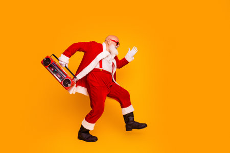 Santa in red suit with a boombox dances on bright orange background for christmas eve party and holiday celebrationの写真素材