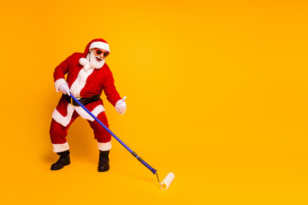 Santa in red suit paints a bright yellow wall with a roller giving a thumbs up enjoying a playful festive momentの写真素材
