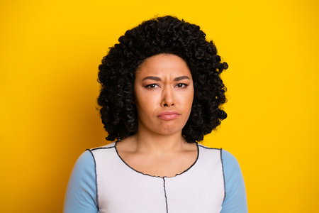 Portrait of a stylish young woman with curly hair displaying a quirky expression against a vibrant yellow backgroundの写真素材