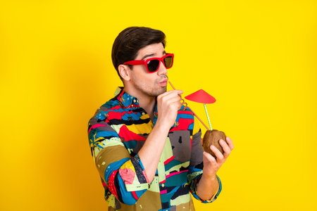 Bright summer man drinks from coconut with umbrella on yellow background fashion modelの写真素材