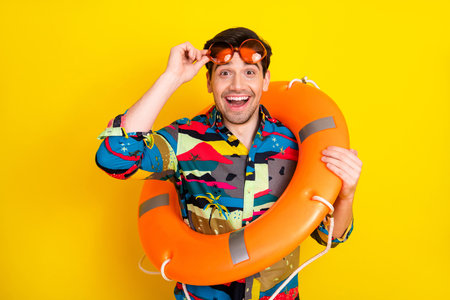 Young handsome brunet man in a colorful shirt with sunglasses and an orange life ring smiling...