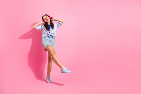 Young woman with headphones dancing against pink background showcasing trendy fashion and a joyful...