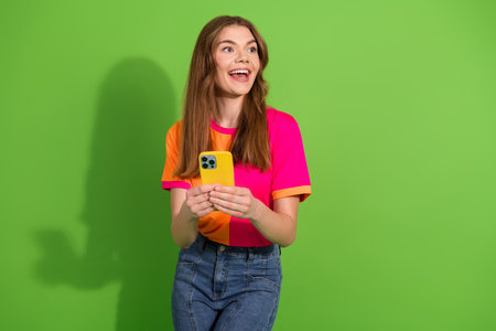 Young female smiling holding yellow smartphone wearing bright pink and orange shirt against vivid...