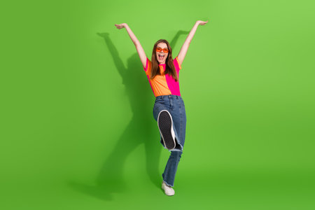 Young woman joyful jump in bright colorful outfit against green background for fashion leisure lifestyle image suitable for advertising and promotionの写真素材
