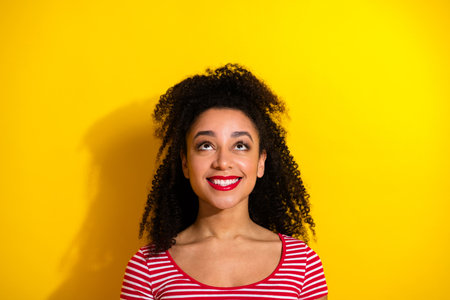 Smiling Woman with Curly Hair Standing Against Yellow Background in Striped Shirt and Bright Red Lipstickの写真素材