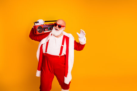 Santa in red costume with white fur and a retro boombox poses against a bright yellow background for festive Christmas stock imageの写真素材