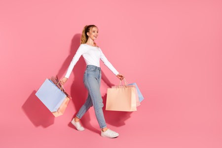 Young fashionable girl smiling and carrying colorful shopping bags on pink background for lifestyle and fashion conceptsの写真素材