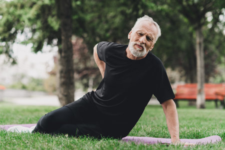 Senior man exercises outdoors in park on a yoga mat stretching a side body on a calm sunny day for fitness and wellbeingの写真素材