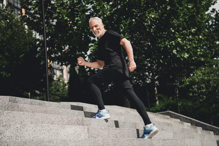 Older man in black athletic wear runs up outdoor stairs in a park city setting showcasing fitness...