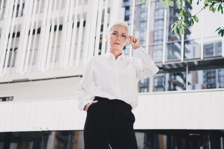 Elegant retired businesswoman walking through modern city streets exuding confidence and...
