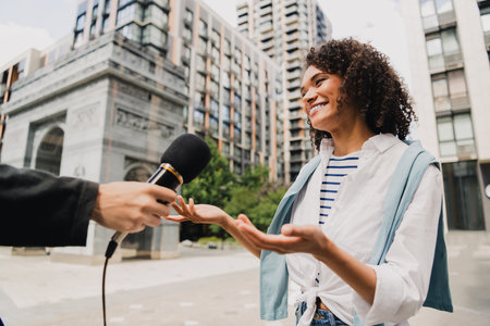 Smiling woman in striped shirt being interviewed on an urban street with microphone reporter and...
