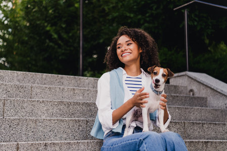 Happy woman with dog sits on outdoor stairs in the city park enjoying a sunny day