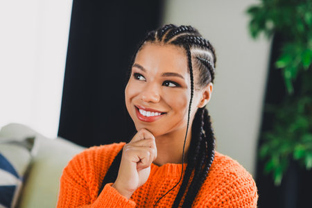 Portrait of a happy young mixed race woman in an orange knit sweater in a cozy living room for lifestyle and fashion stock photoの写真素材