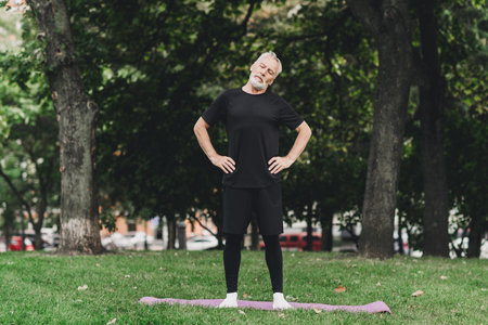 Healthy active man in park doing a standing chest stretch on a yoga mat outdoorsの写真素材