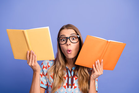 Young woman with glasses holds colorful notebooks and shows surprised expression while posing for fashion lifestyle imageの写真素材