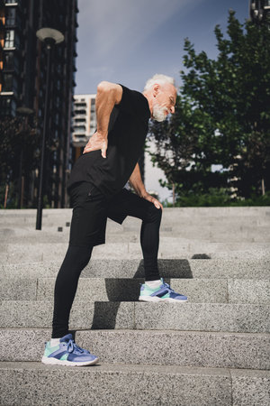 Elderly bearded man in athletic wear climbs concrete stairs outdoors in the city park showing fitness health and determination for lifestyle stock photoの写真素材
