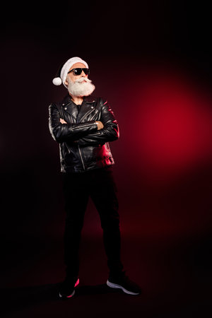 Cool Santa rocker in leather jacket and Santa hat with beard and sunglass in dramatic red lighting for holiday fashion and Christmas contentの写真素材