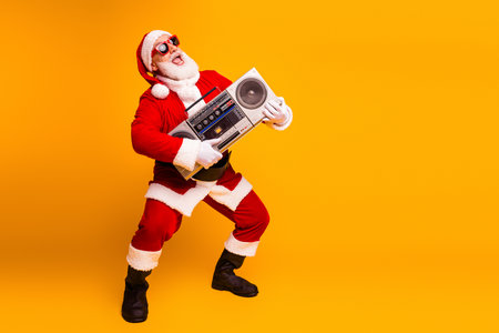 Santa in red suit with white fur trim dances and holds a retro boombox in a bright orange studio creating a fun festive christmas moodの写真素材