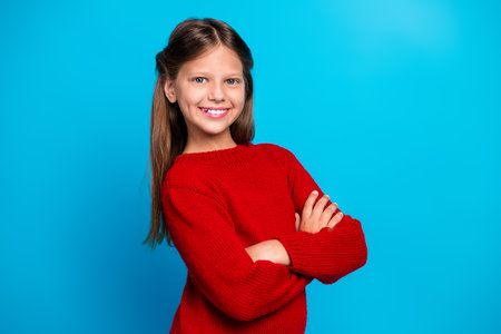 Confident girl in red sweater stands with arms crossed against a bright blue background for festive Christmas themed stock imageの写真素材