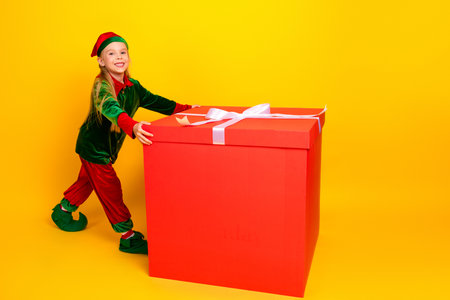 Festive Christmas elf character with a giant red gift box in a bright yellow setting, perfect for holiday advertisingの写真素材