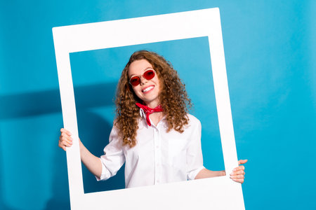 Photo portrait of nice young lady sunglass hold instant photo frame wear trendy white garment isolated on blue color backgroundの写真素材