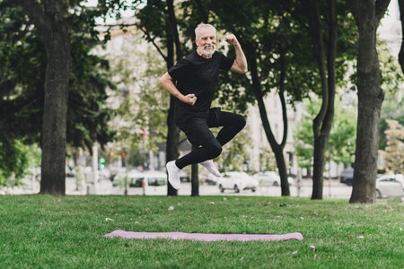 Energetic senior man jumps in the park during outdoor fitness session on a pink mat showcasing health energy and active lifestyleの写真素材