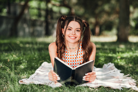 Young girl reading a book in the park on a sunny day enjoying a peaceful outdoor moment in casual stylish outfitの写真素材